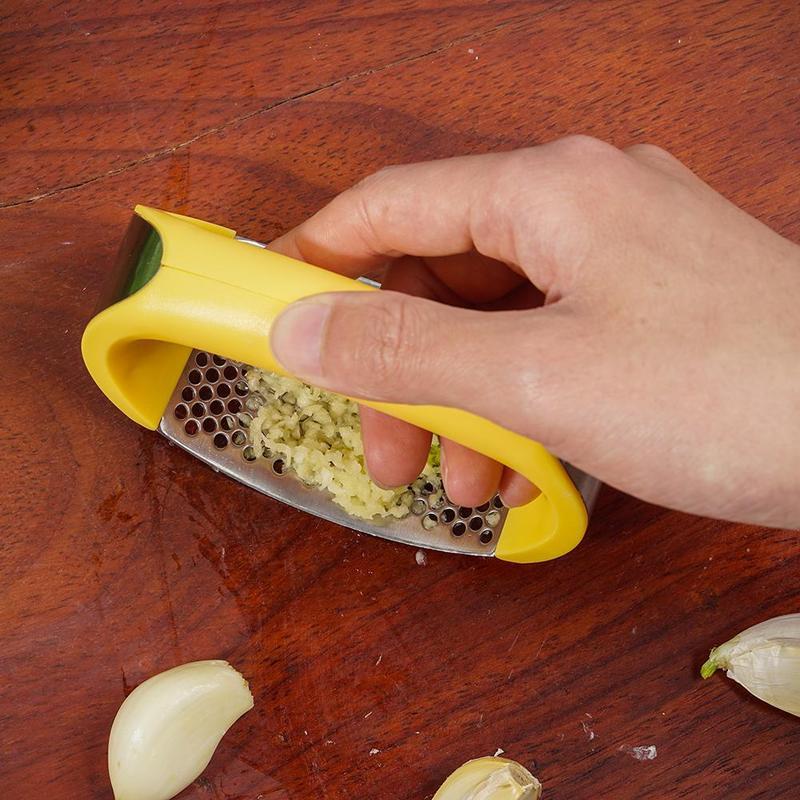 Hand using a garlic press on a wooden surface with garlic cloves around.