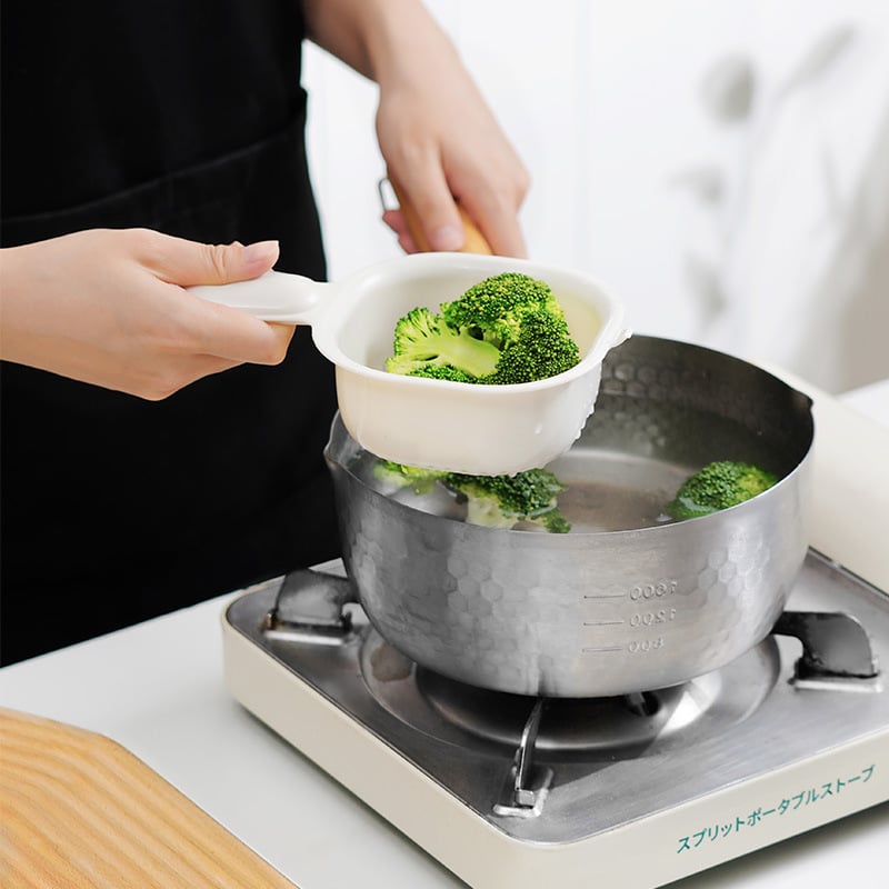 Person adding broccoli into a pot of water on a stove